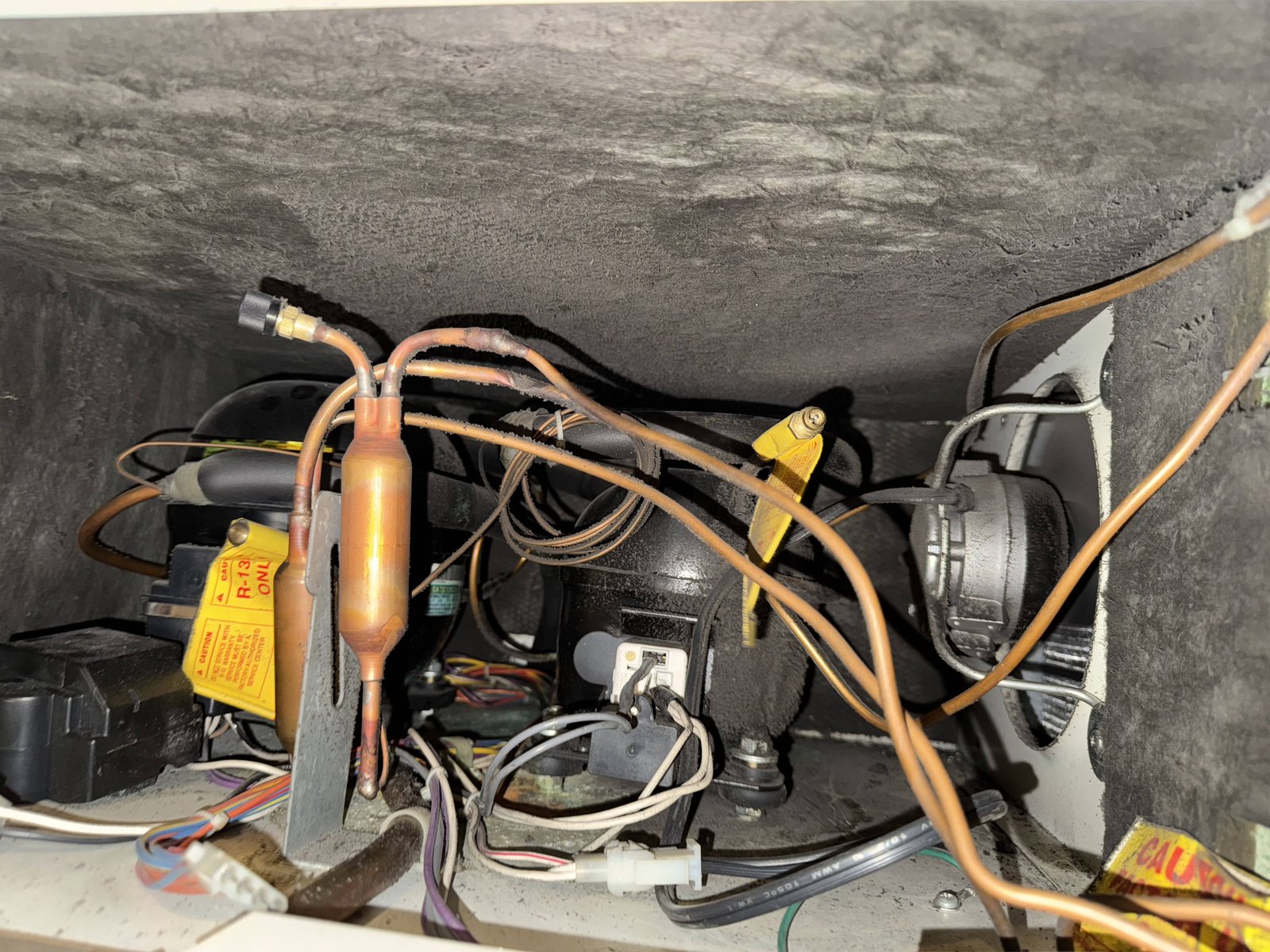 Sub-Zero compressor compartment with R-134a refrigerant, copper suction and discharge lines, filter-drier and process tube — sealed system component being inspected during NYC service call